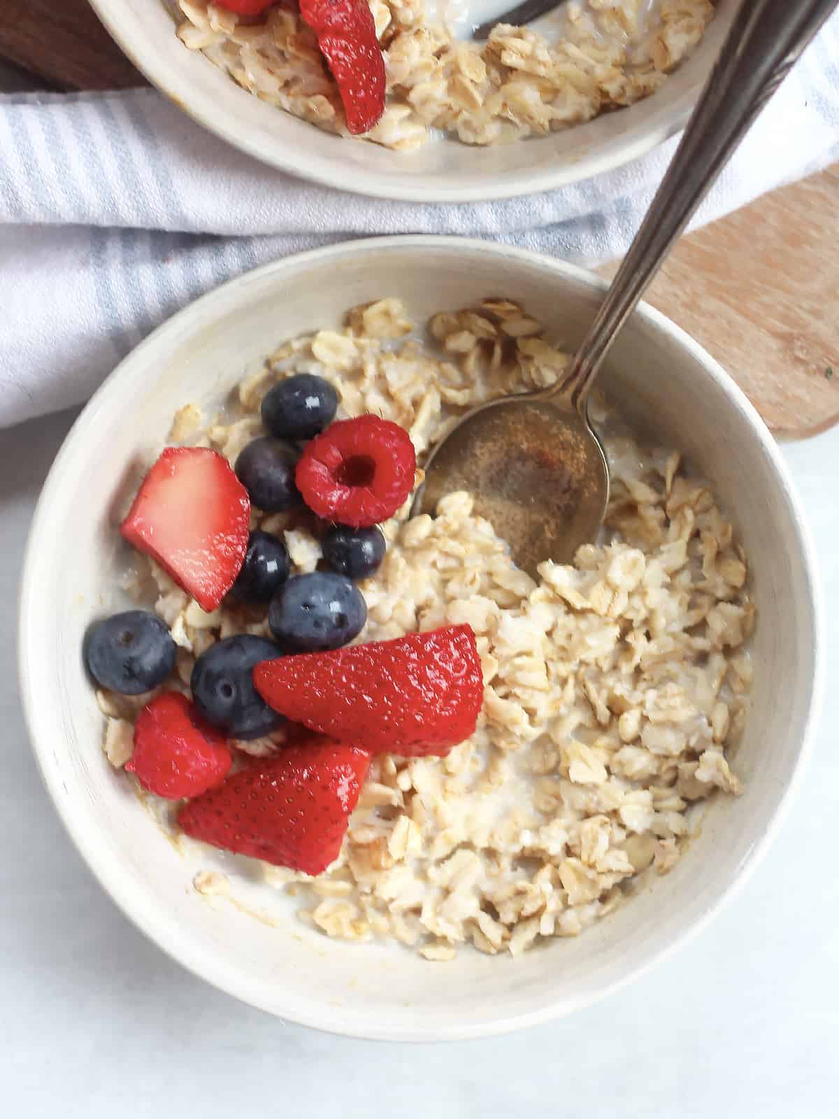A spoon in a bowl of oatmeal topped with fresh berries.