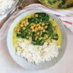 A bowl of yellow chickpea and spinach curry served with rice.