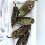 Four air fryer roasted jalapenos on a white plate.