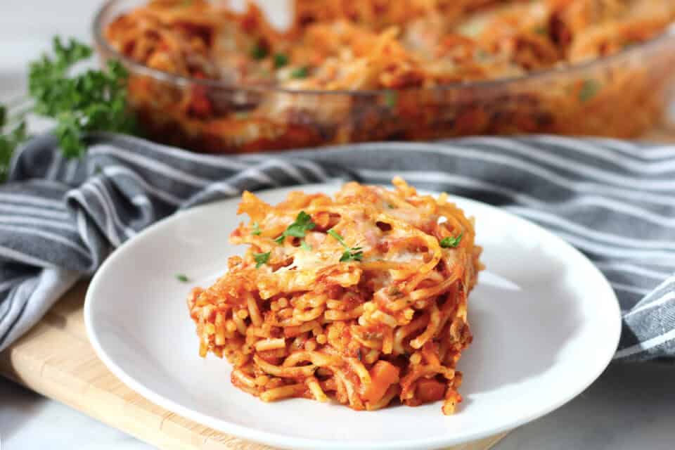 Spaghetti gratin served on a white plate with fresh parsley garnish.