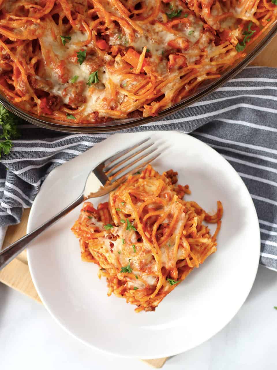 A square of baked spaghetti bolognese served on a white plate with a fork.