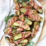 Bacon wrapped pickles on a serving plate with fresh dill garnish.