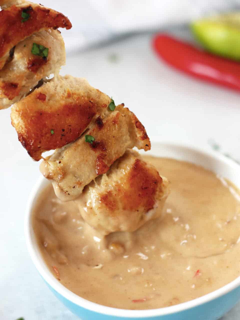 A chicken skewer being dipped in peanut sauce.