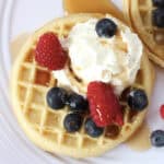 Raspberries, blueberries, whipped cream and maple syrup on a waffle.