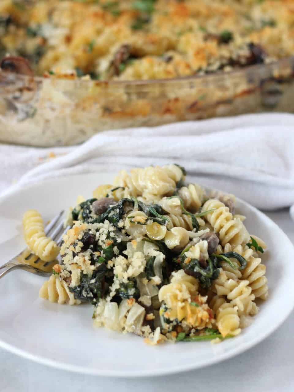 Pasta with creamy sauce, mushrooms and spinach served on a white plate.