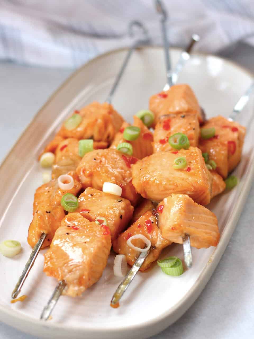 Cubes of salmon on metal skewers served on a white plate.