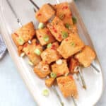 Salmon skewers with red chilies garnished with green onion.