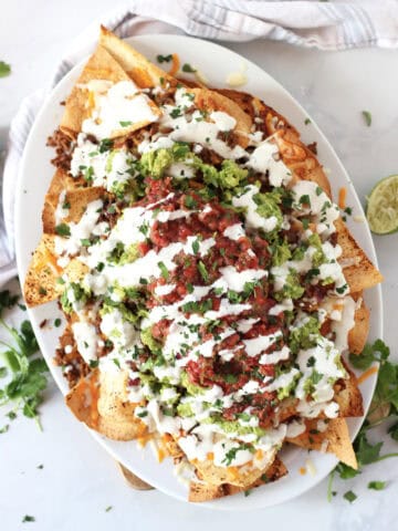 Chili beef nachos served on a white platter with toppings.