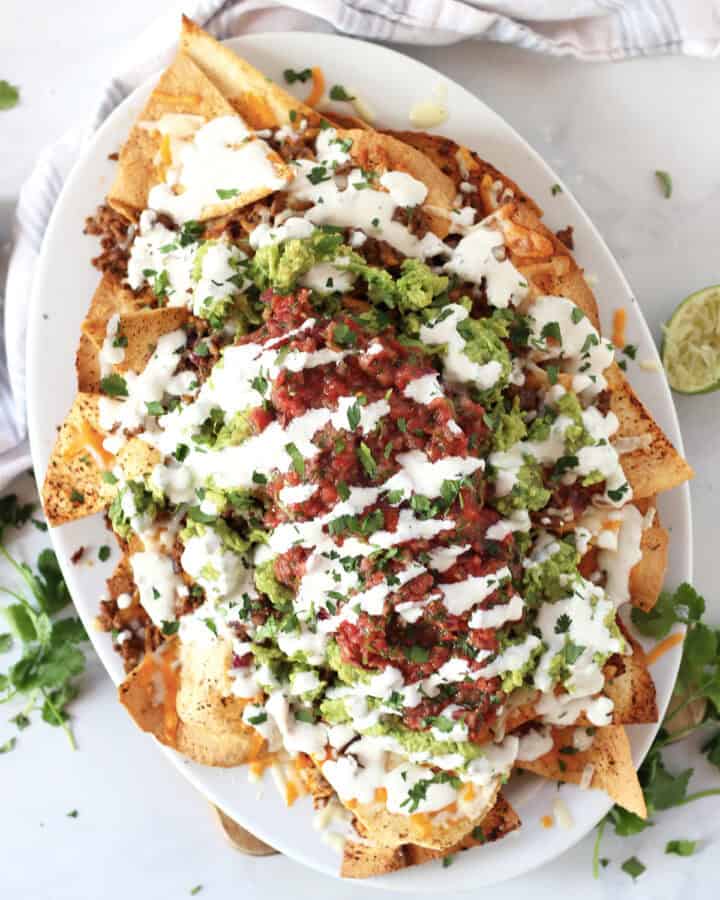 Chili beef nachos served on a white platter with toppings.