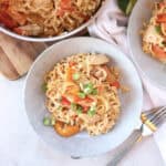 Noodles, chicken and vegetables served in a bowl next to two forks.