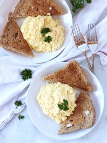 Two plates with scrambled eggs and toast.