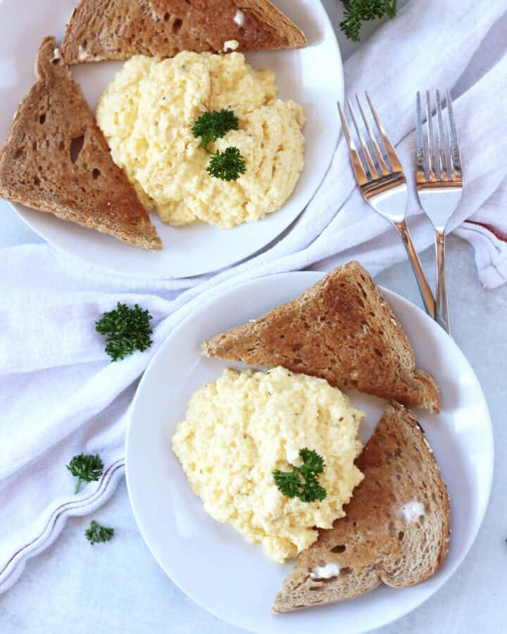 Two plates with scrambled eggs and toast.