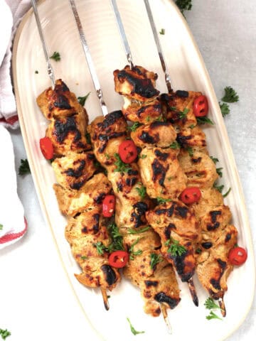 Four tandoori chicken kabobs on metal skewers.