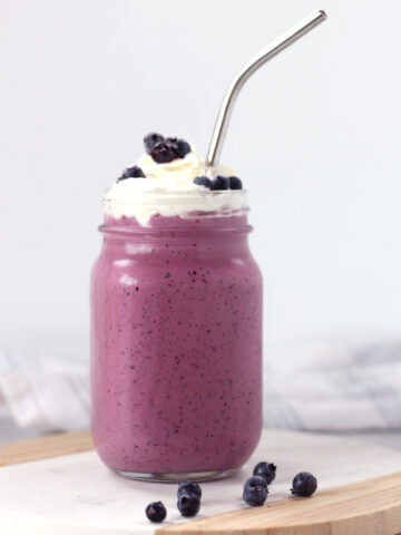 A metal straw in a tall glass of purple milkshake.