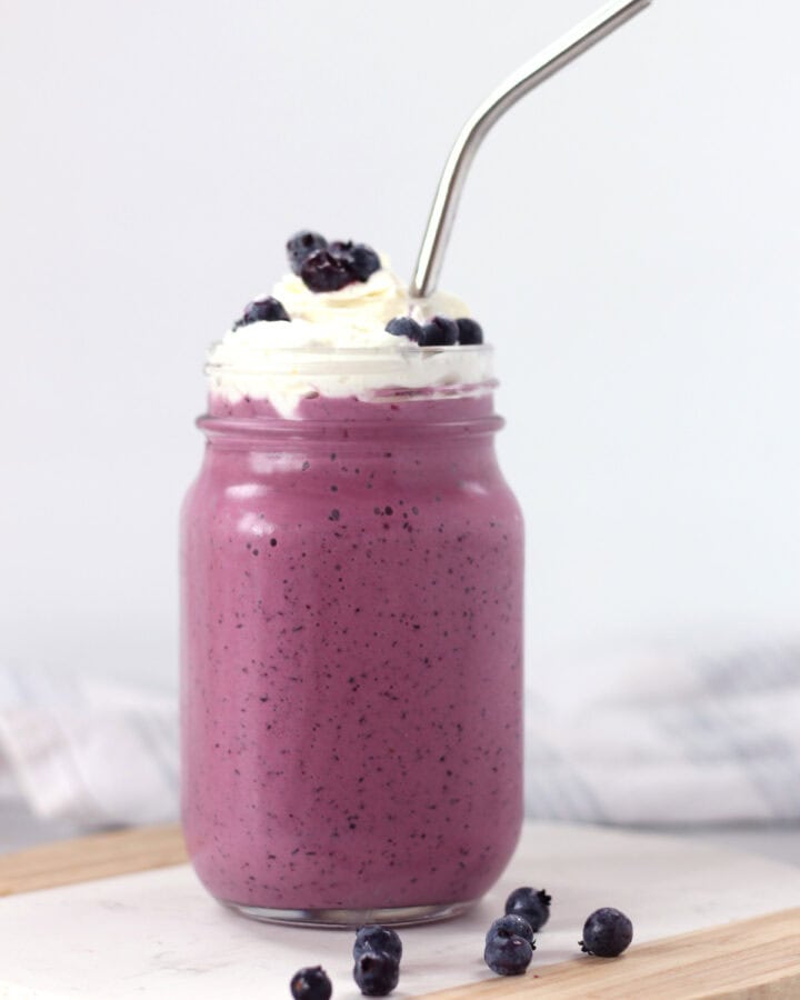 A metal straw in a tall glass of purple milkshake.