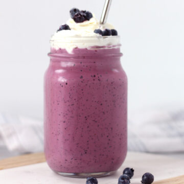 A blueberry milkshake in a glass with whipped cream topping.