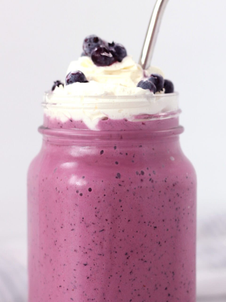 Whipped cream topping and fresh blueberries on top of a poured milkshake.