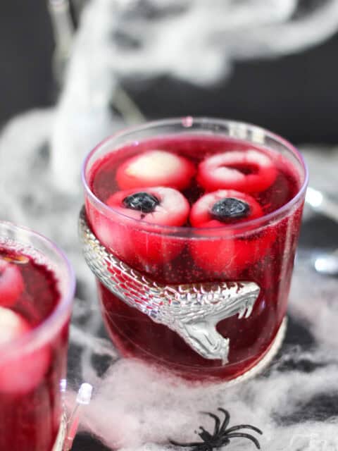Halloween punch with eyeballs served in a glass decorated with a silver snake.