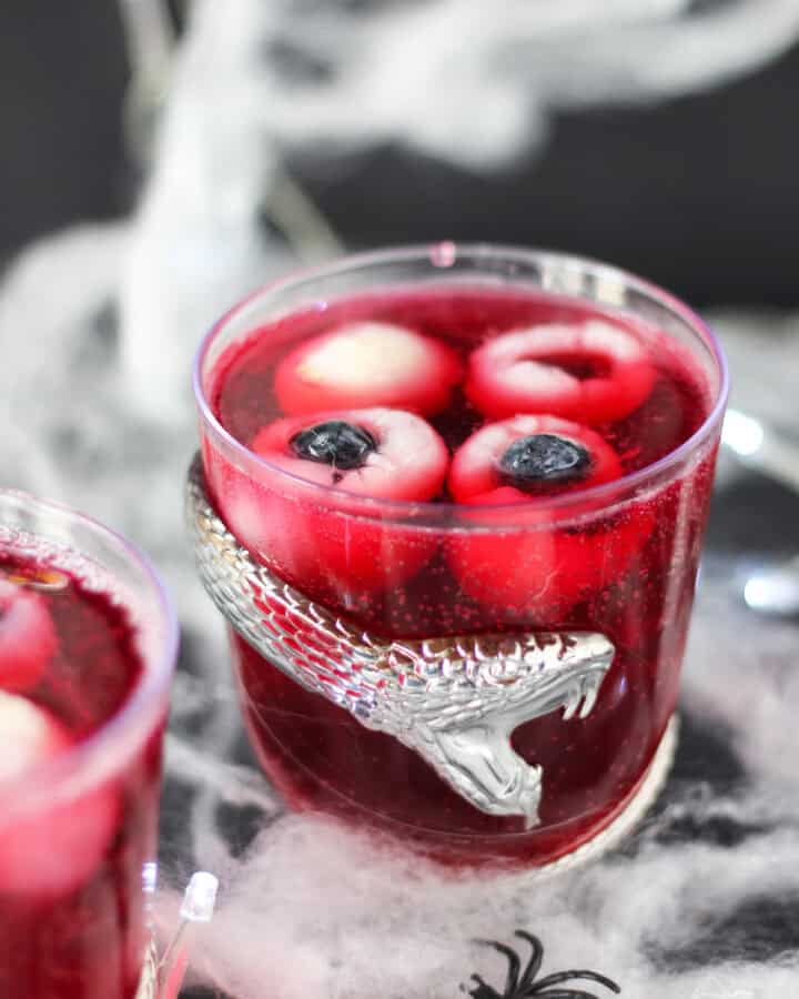 Halloween punch with eyeballs served in a glass decorated with a silver snake.