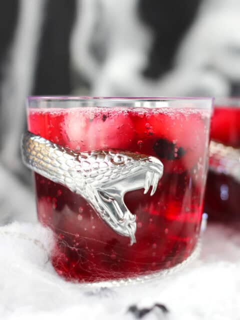 Red punch served in a spooky glass with a snake wrapped around it.