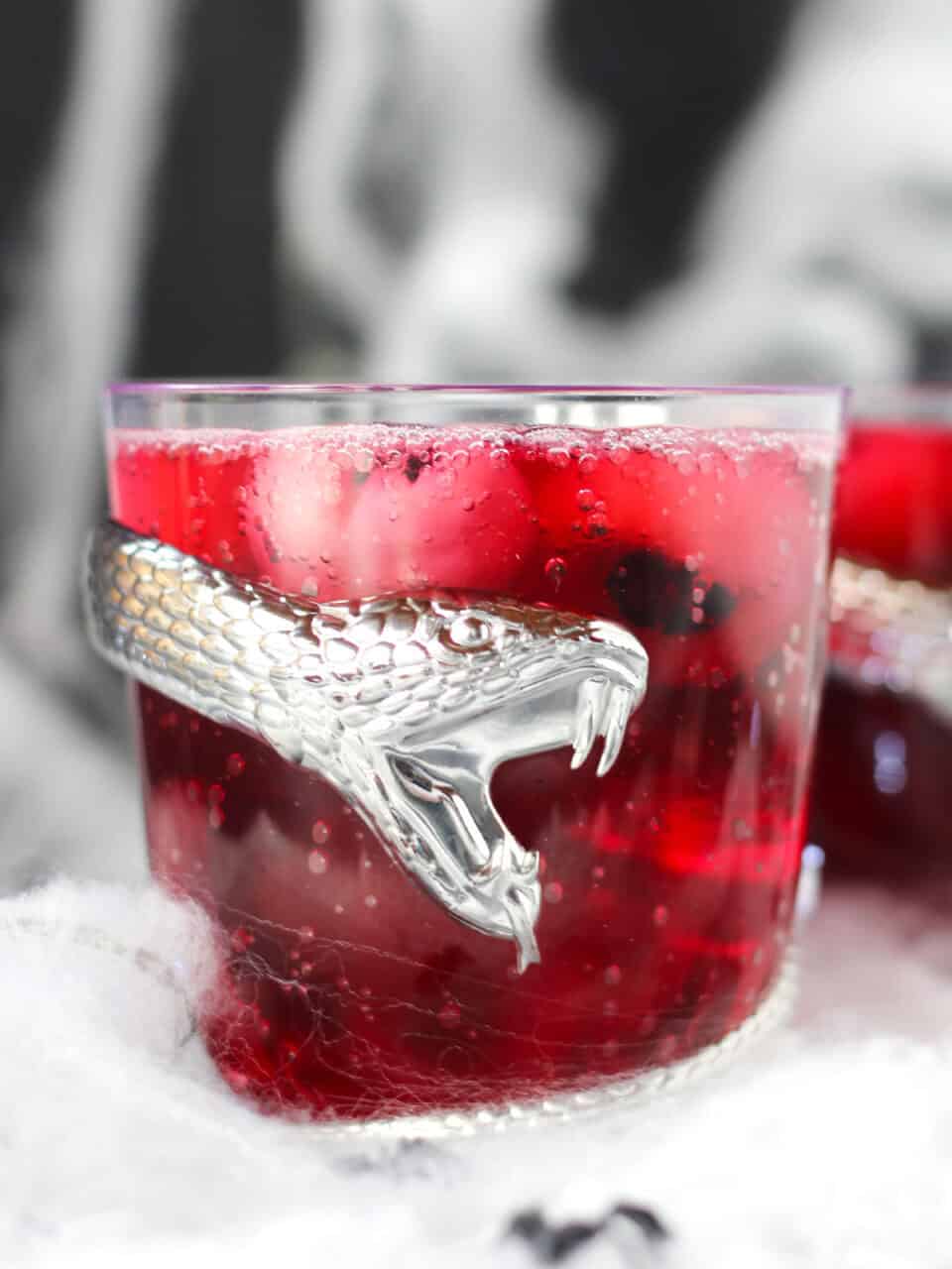 Red punch served in a spooky glass with a snake wrapped around it.