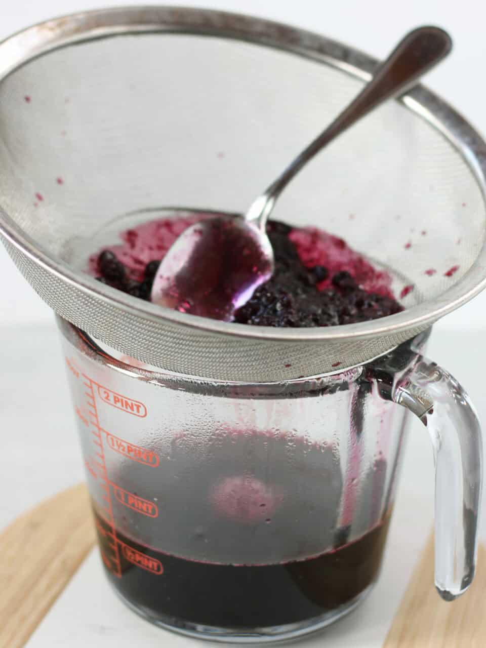Using a fine mesh sieve to strain the blueberries.