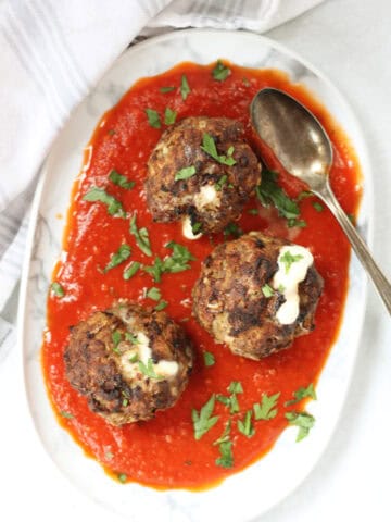Three meatballs served on a plate with red sauce.