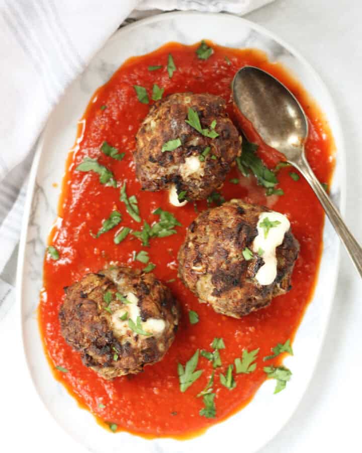Three meatballs served on a plate with red sauce.