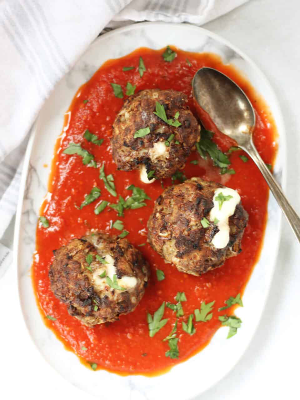 Three meatballs served on a plate with red sauce.
