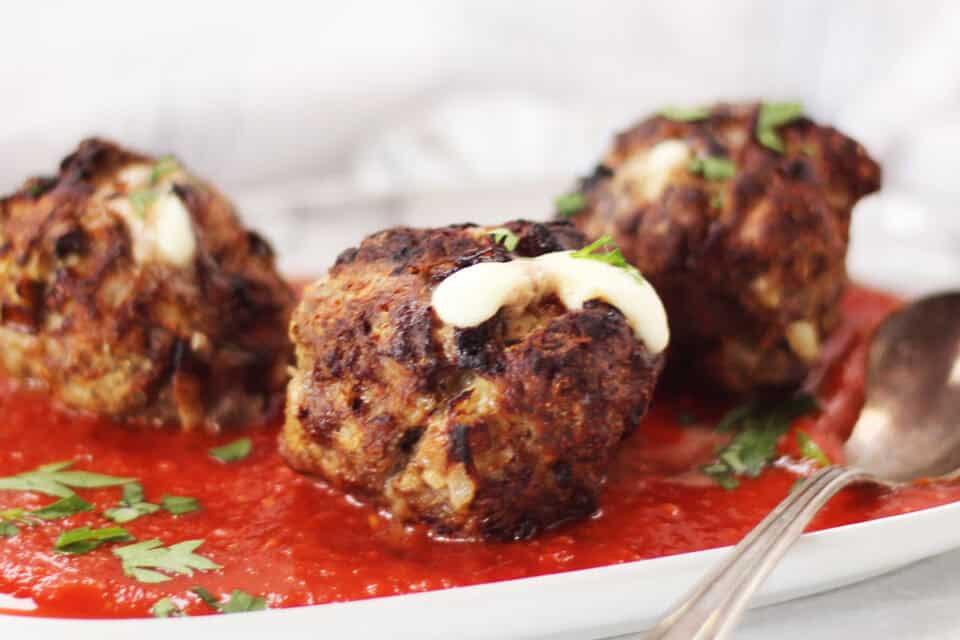 Three stuffed meatballs served on a plate with marinara sauce.