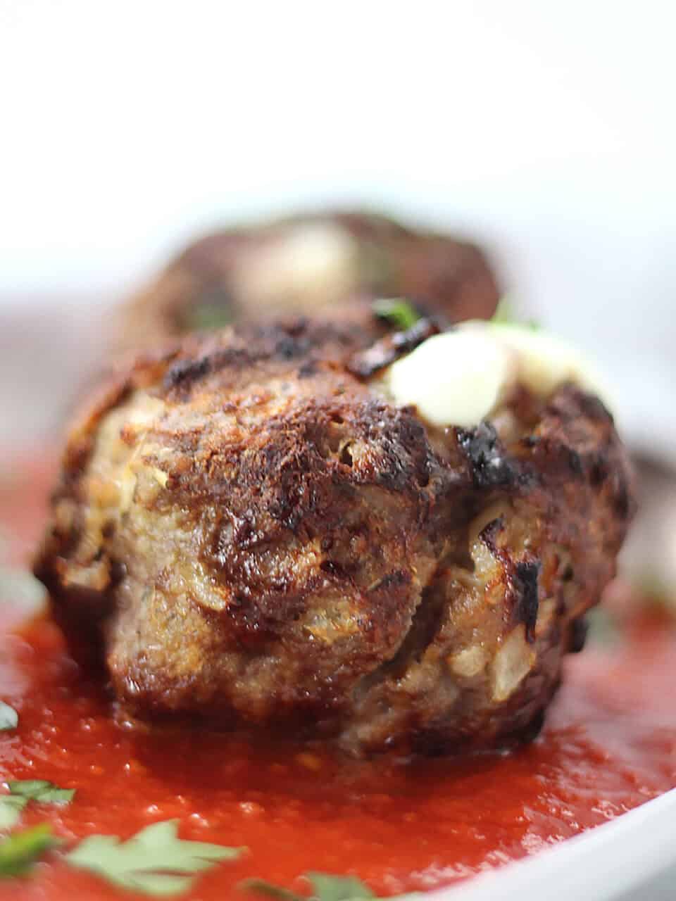 An air fried beef meatball with cheese served on top of red sauce.
