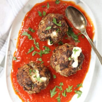 Three cheesy meatballs served with marinara sauce.