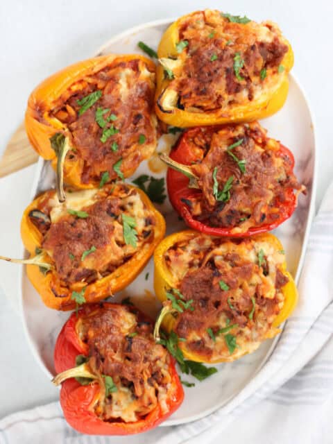 Six stuffed bell peppers on a plate garnished with fresh parsley.