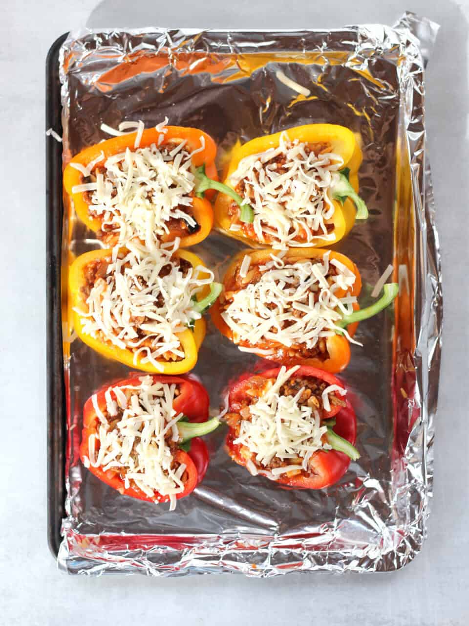 Uncooked stuffed peppers on a foil lined baking sheet.