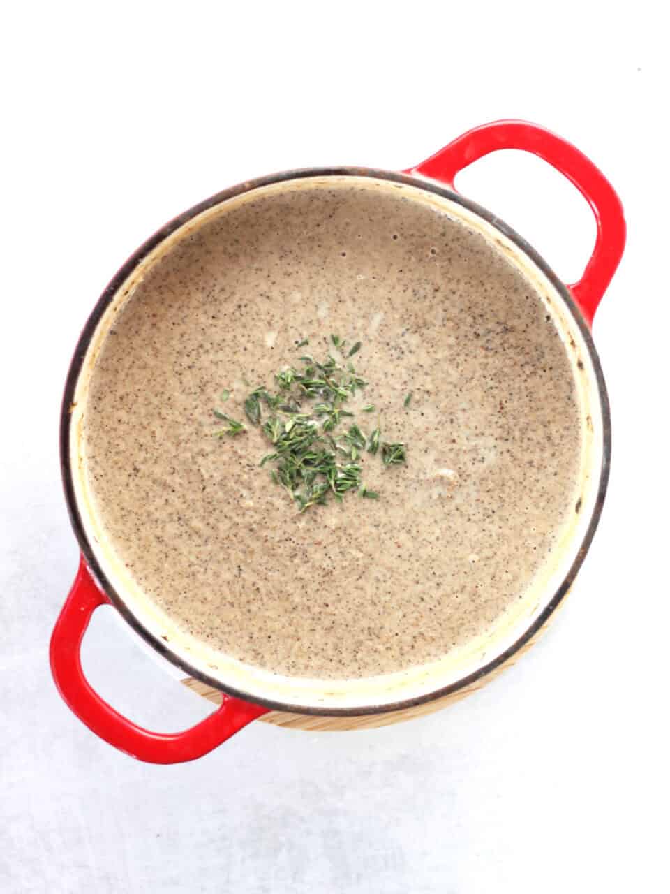 Blended soup in a red stock pot garnished with fresh thyme leaves.