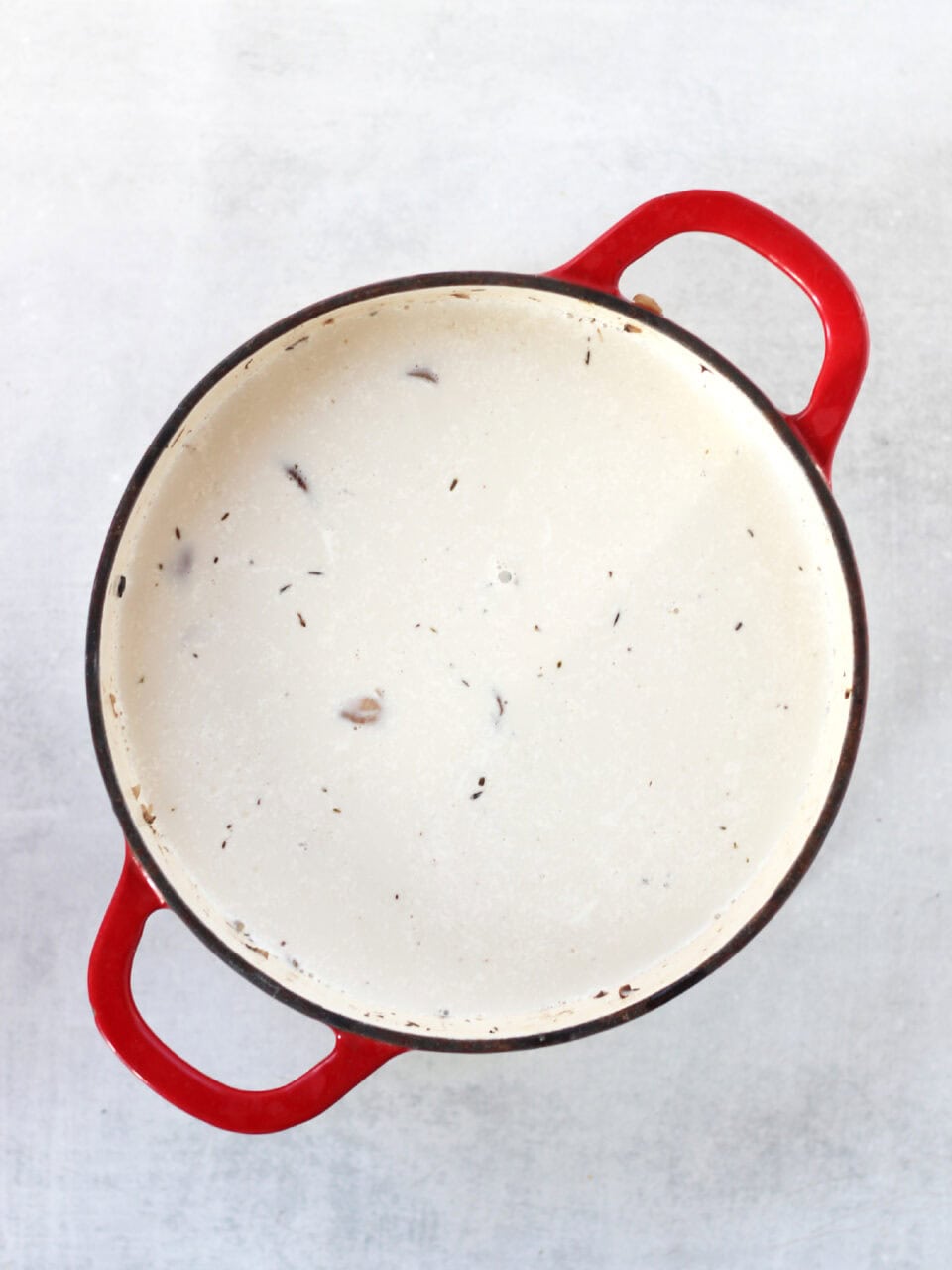 A red stock pot with creamy liquid in it.