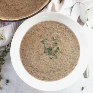 Garlic mushroom soup served in a white bowl next to a spoon.