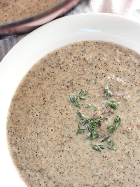 Creamy mushroom soup in a white bowl garnished with thyme leaves.