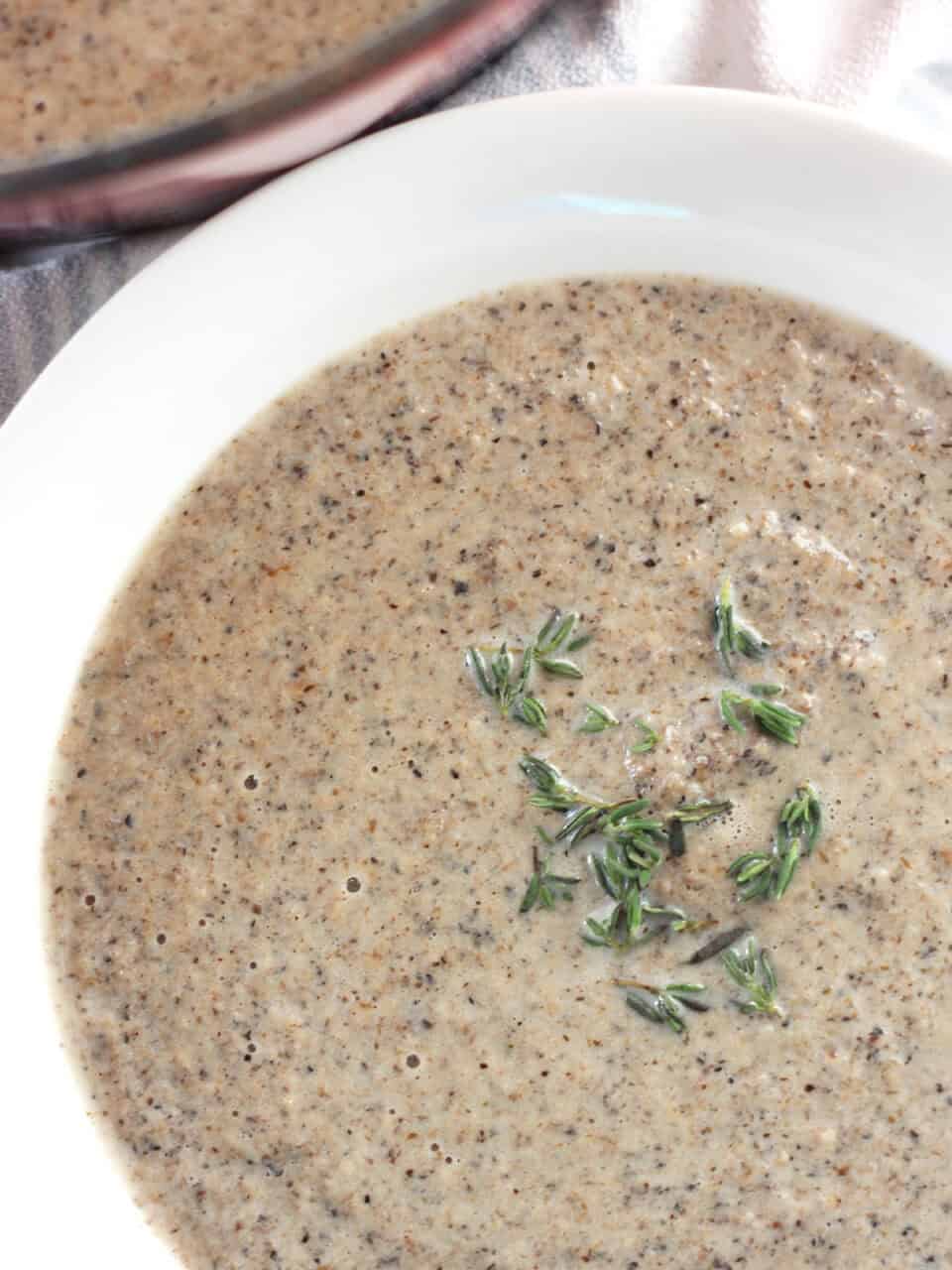 Creamy mushroom soup in a white bowl garnished with thyme leaves.