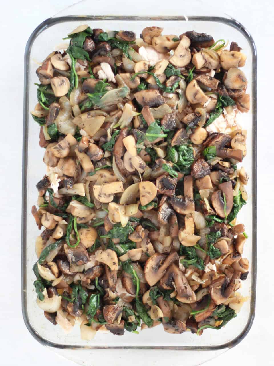 Cooked mushrooms and spinach in a glass baking dish.