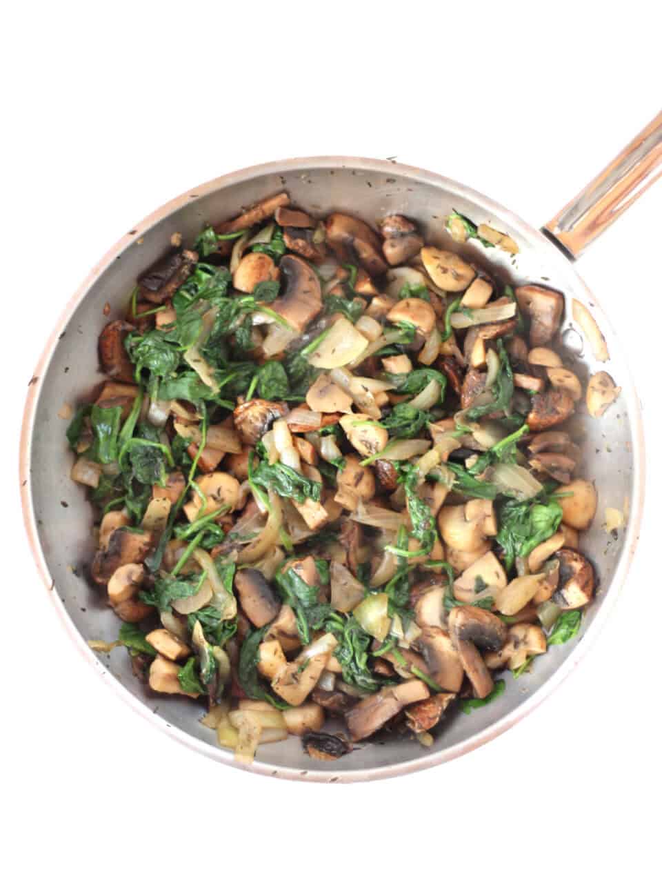 Sauteed mushrooms and spinach in a silver skillet.