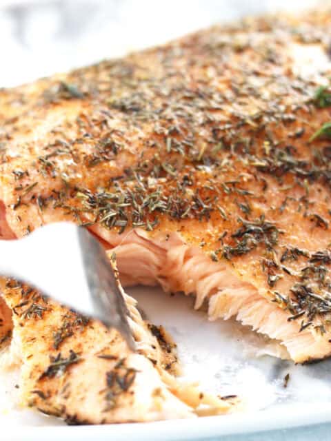 A fork cutting the salmon to reveal flaky flesh.