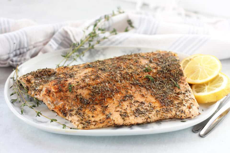 Cooked salmon fillet with herb topping on a white serving plate.