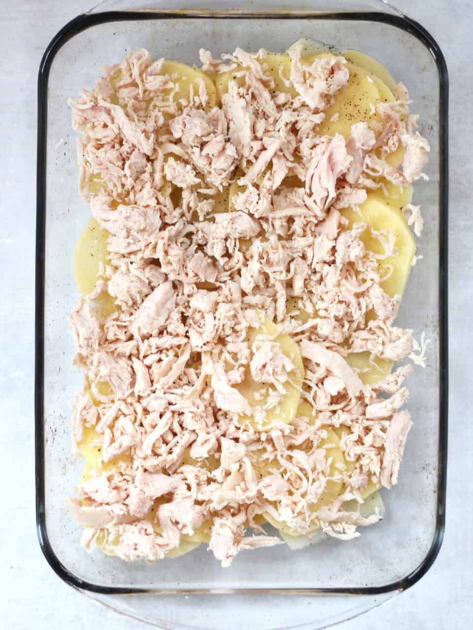 Shredded chicken layered on top of potatoes in a glass dish.