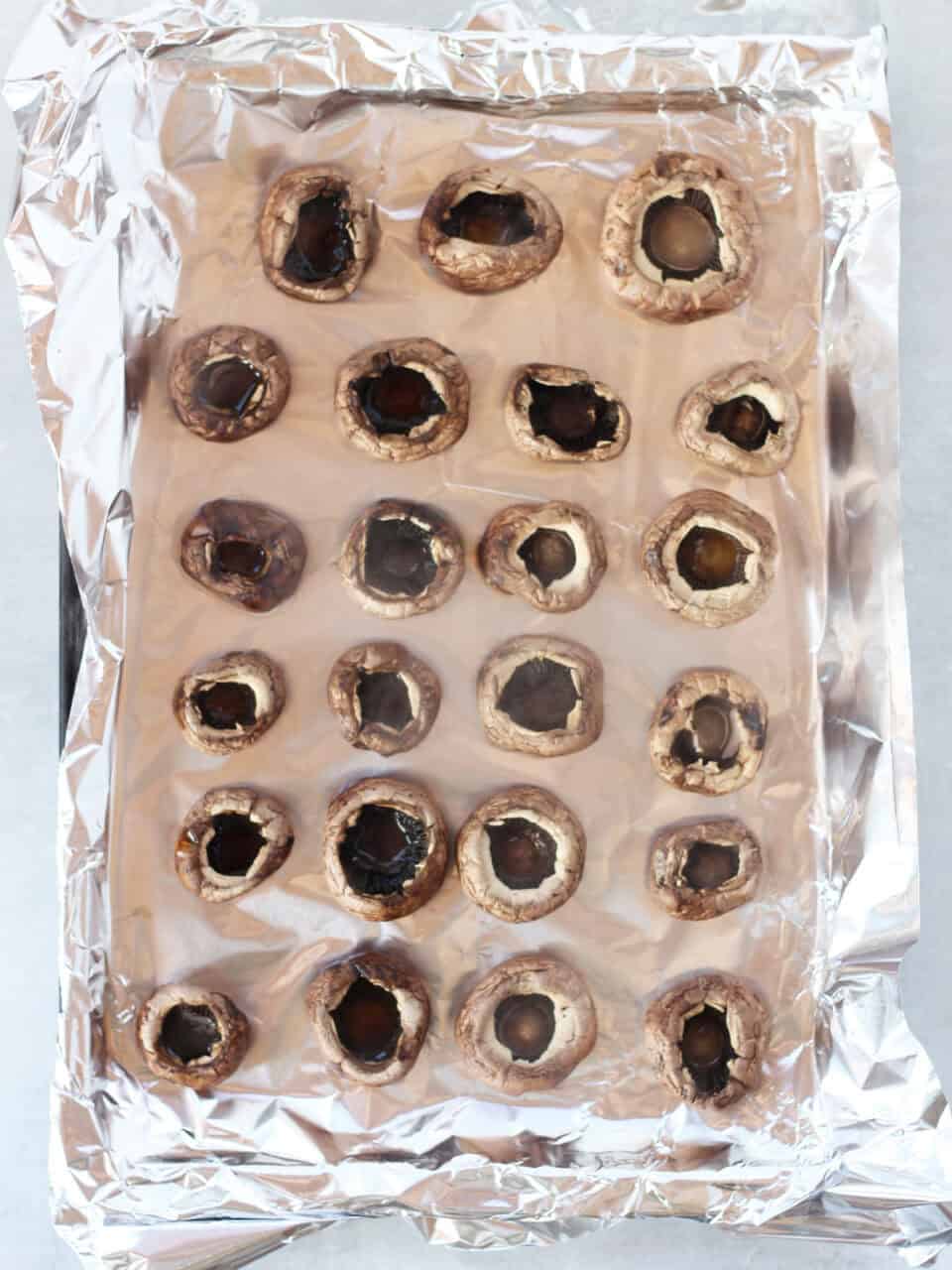 Cleaned mushrooms on a foil lined tray with stems removed.