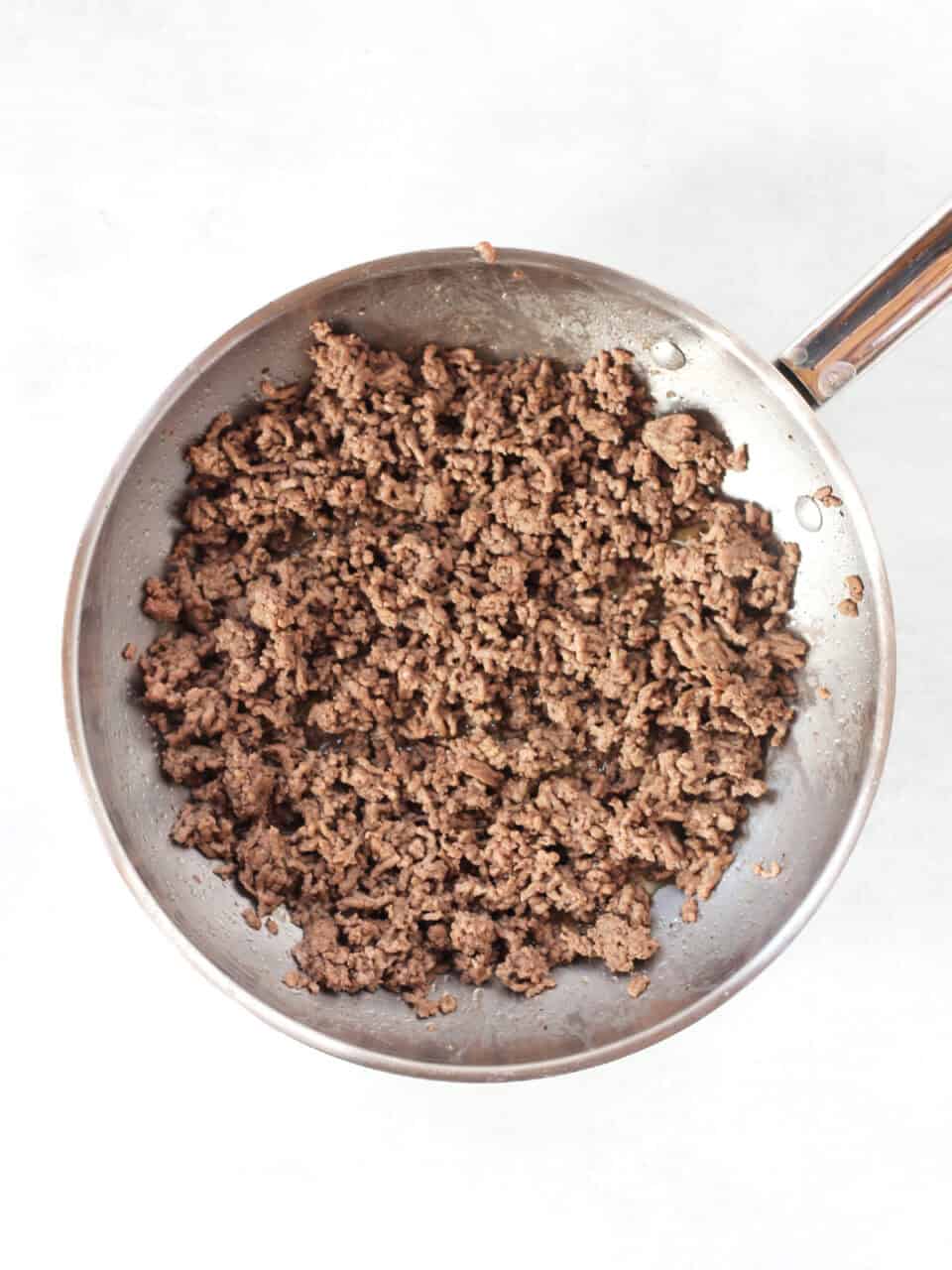 Browned ground beef in a silver skillet.