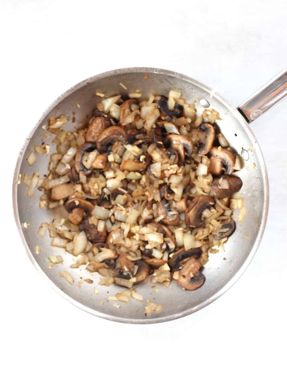 Browned mushrooms and onions in a silver skillet.
