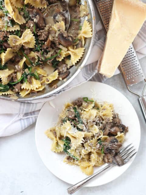 A plate of beef pasta served up from a skillet next to a block of parmesan cheese.