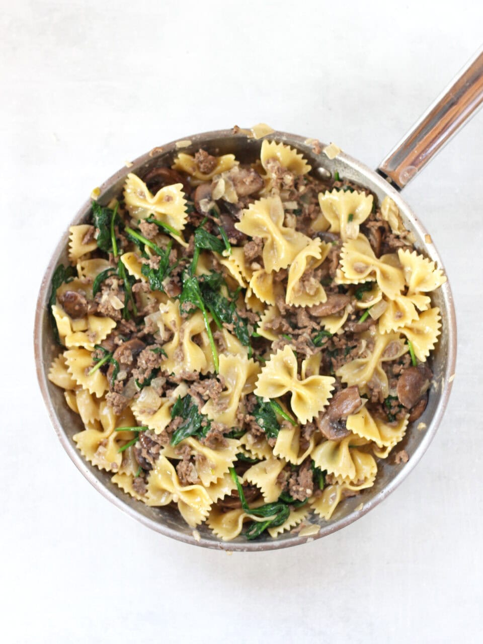 Cooked pasta and spinach mixed into the mushrooms in a silver skillet.