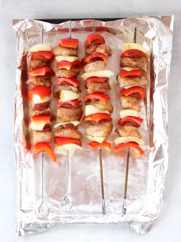 Uncooked chicken skewers on a foil line baking tray.
